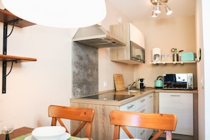 A compact kitchen with a microwave, stove, and a small refrigerator. There are wooden chairs and a table with a green placemat. - Apartment Caroline with Pool & Sauna (Schluchsee)
