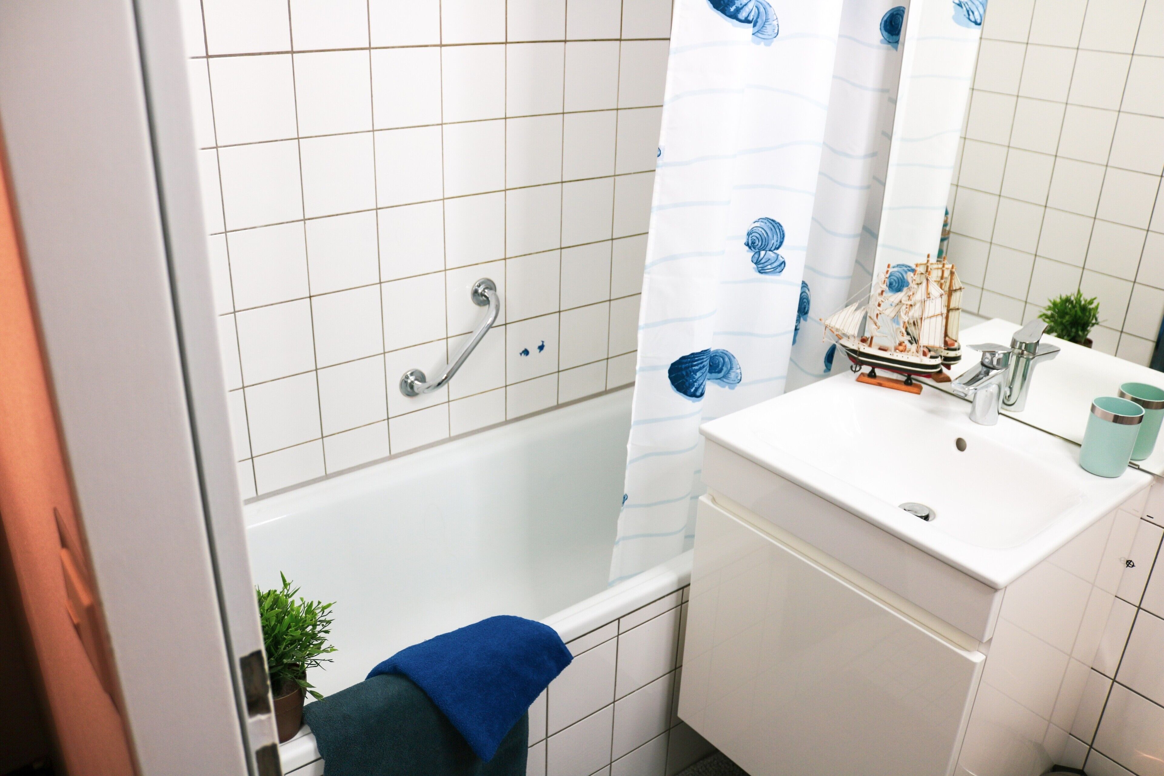 A bathroom with a bathtub, a white sink, a mirror, and a ship model on the sink.