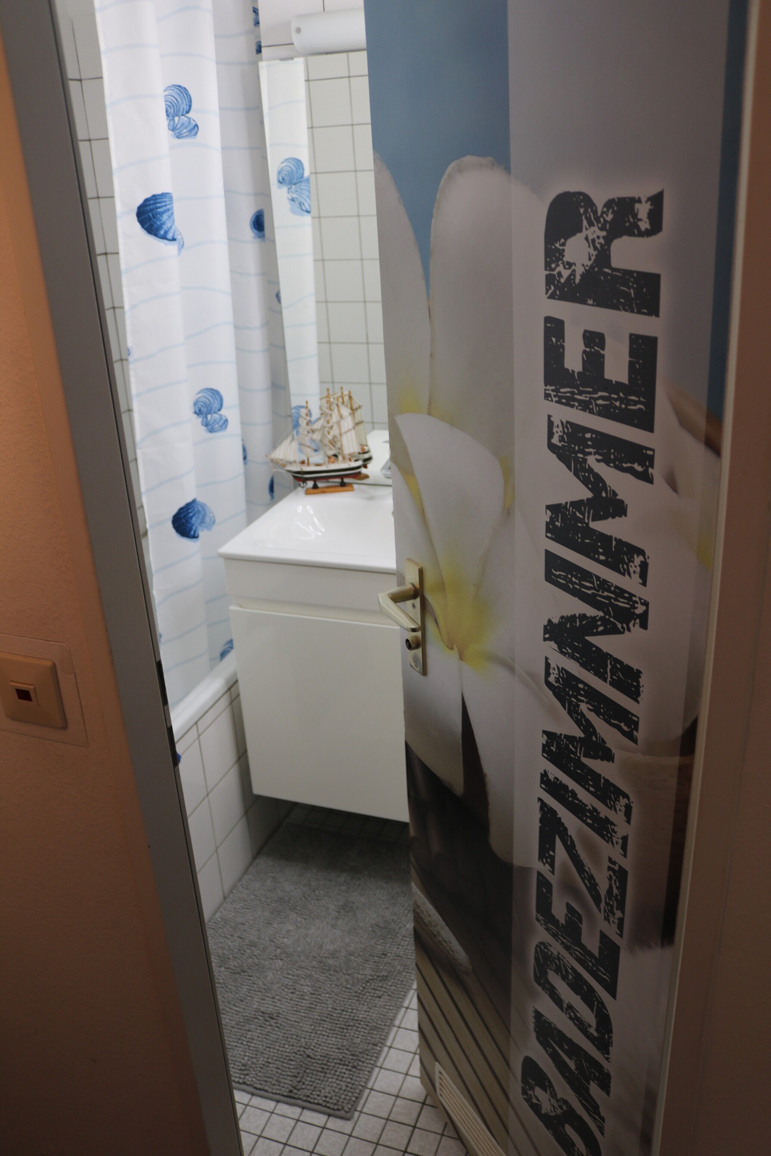 A narrow bathroom with a white sink, a ship model on the counter, and a towel rack.