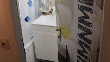 A narrow bathroom with a white sink, a ship model on the counter, and a towel rack.