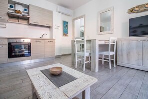 A modern kitchen with a built-in oven, white cabinetry, and a dining area with a table and chairs. - GuestHost - A comfortable and welcoming 55 square meter apartment, perfect for two people, located on the ground floor of a modern condominium with a shared pool in the beautiful town of Palau, ideal for enjoying a relaxing stay.The property is located a (Palau)