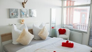 Hotellihuone, jossa on sänky, valkoiset vuodevaatteet, punainen sydämenmuotoinen tyyny ja taideteos seinällä.