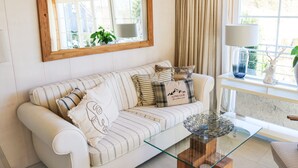 A white sofa with striped cushions, a glass coffee table, a wooden-framed mirror, and a window with curtains. - Villa Wolfsgrund – 5-Star Luxury Design Holiday Home (Schluchsee)