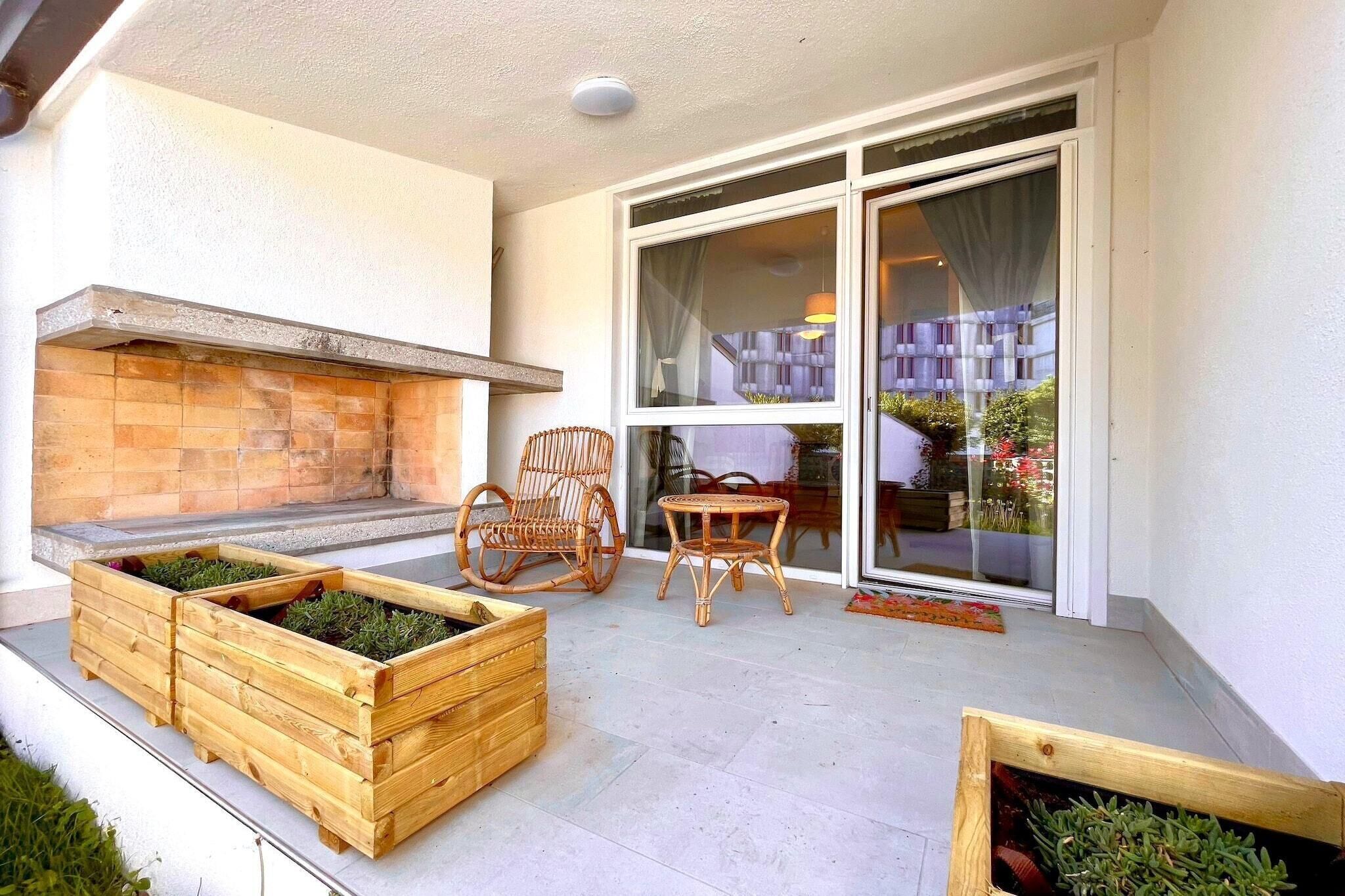 An outdoor patio with a built-in fireplace, wooden planters, wicker chairs, and a glass door leading to a balcony.