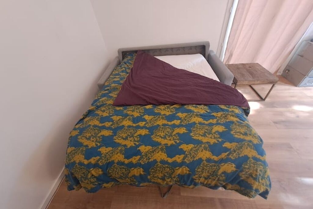 A single bed with a patterned bedspread, a pillow, and a wooden side table.
