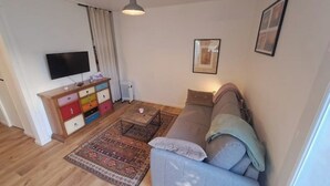 Un salon avec un canapé, un téléviseur, un meuble aux couleurs vives et un tapis à motifs.