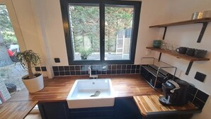 Une cuisine moderne dotée d’une grande fenêtre, de plans de travail en bois, d’un évier blanc et d’une machine à café.