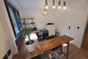 A compact kitchen with a wooden table, a potted plant, and modern pendant lighting.