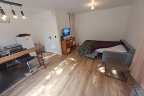 A compact room with a bed, a small desk, a television, and a kitchenette.