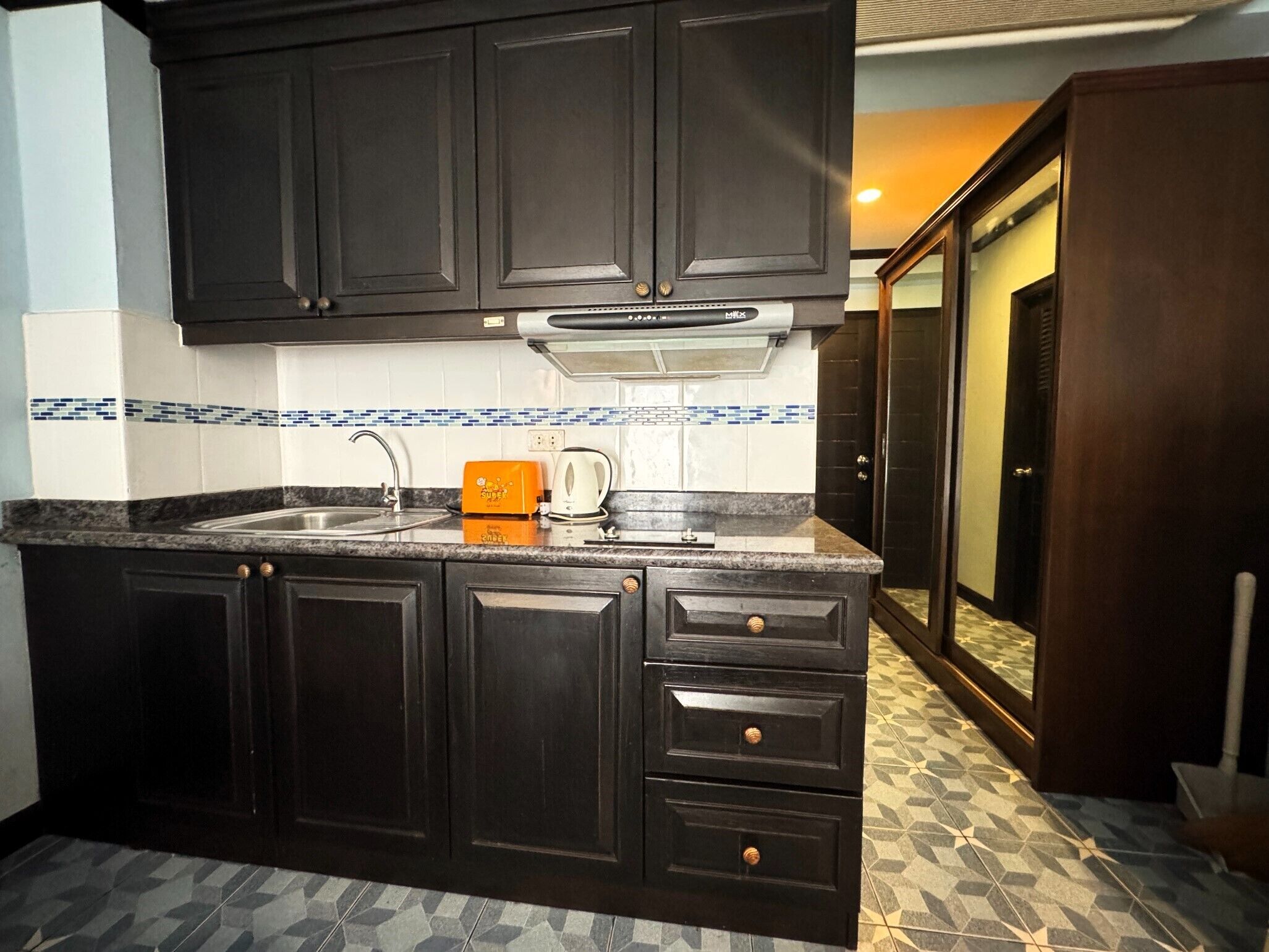 A kitchen with dark cabinets, a granite countertop, a sink, and a coffee maker.