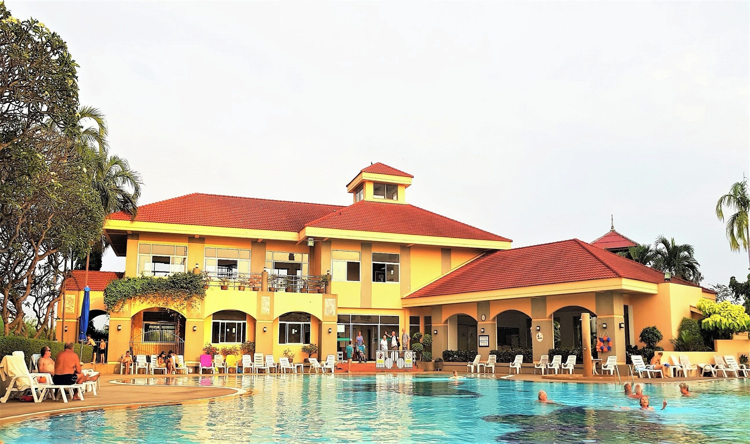 A large resort building with a swimming pool, multiple balconies, and outdoor seating areas.