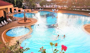A large indoor swimming pool with multiple lanes, surrounded by lounge chairs and a small garden area. - Studio Condo Close Jomtien Beach - Jomtien Beach Condominium A3 (Pattaya)