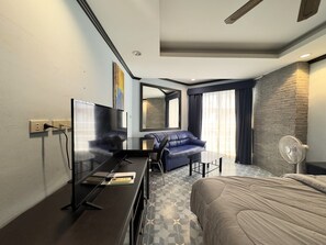A modern hotel room with a large bed, a sofa, a desk with a flat-screen TV, a mirror, and a large window with curtains. - Studio Condo Close Jomtien Beach - Jomtien Beach Condominium A3 (Pattaya)