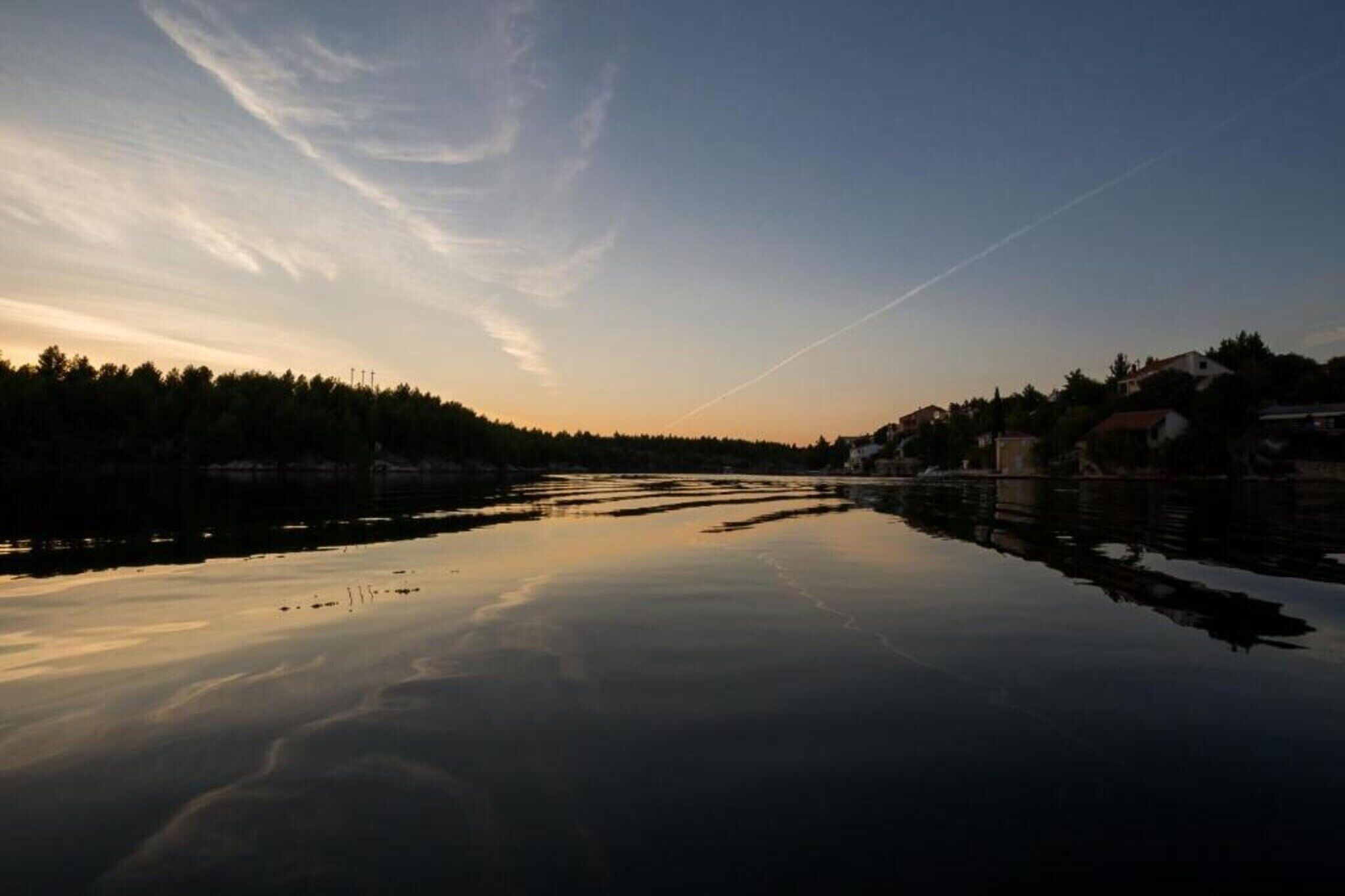 A calm river reflecting the sky with a distant shoreline and trees.