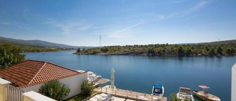 Zona de piscina con sillones de descanso, un bote pequeño y vistas a un lago y colinas.