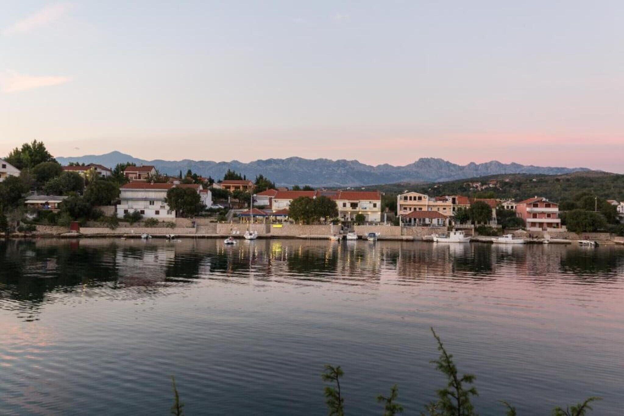 Blick auf das Wasser mit Gebäuden, einem ruhigen Fluss und Bergen im Hintergrund.
