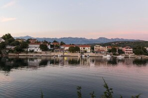 A waterfront view with buildings, a calm river, and mountains in the background. - Pool-view 1-bedroom apartment in Obrovac (Obrovac)