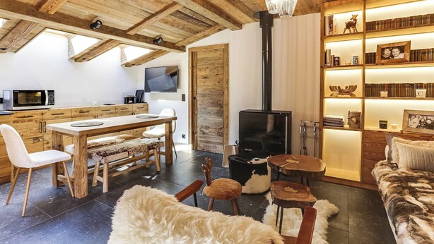Un espacio de estar acogedor con techo de madera, chimenea, mesa de comedor con sillas, sofá y estantería.