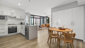 A modern kitchen with white cabinets, a central island, and a dining area with wooden chairs and a table. - Central Apartment with Rooftop Pool & Views (South Brisbane)