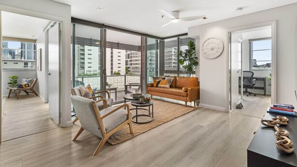 A modern living room with a sofa, armchair, coffee table, and a view of a balcony with a railing. - Central Apartment with Rooftop Pool & Views (South Brisbane)