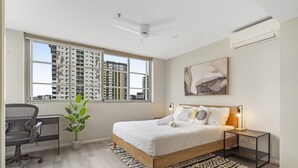 A modern bedroom with a wooden bed, a desk, a potted plant, and a city view through large windows. - Central Apartment with Rooftop Pool & Views (South Brisbane)