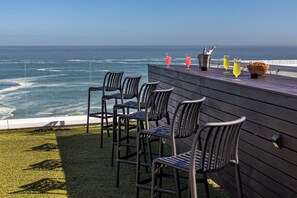 A terrace with four chairs and a wooden table, overlooking the ocean. - Clifton Sea View Duo Penthouse (Cape Town)