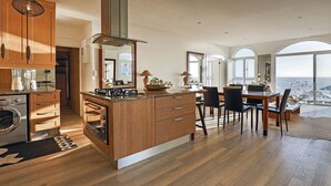 A modern kitchen with wooden cabinets, a central island, and a dining area with a view. - Clifton Sea View Duo Penthouse (Cape Town)
