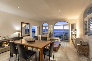 Amplia sala de estar con una mesa de comedor, asientos cómodos y ventanas grandes con vista al mar.