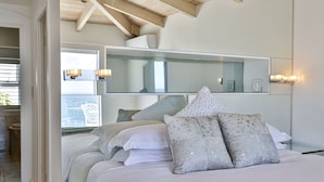 A bedroom with a large bed, a mirrored headboard, and a view of a balcony. - Clifton Sea View Duo Penthouse (Cape Town)