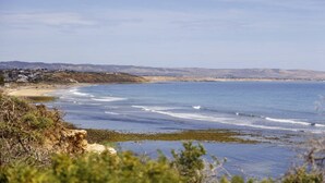 Eine Küstenlandschaft mit Sandstrand, felsigem Ufer und einer in der Ferne liegenden Stadt.
