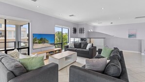 Ein modernes Wohnzimmer mit einer grauen Sofagarnitur, einem Couchtisch und einem Fernseher. Ein großes Fenster bietet Blick auf Gebäude und Grünflächen.