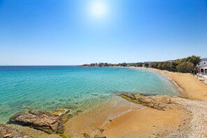 Una playa con aguas turquesas cristalinas, una orilla arenosa y edificios al fondo.