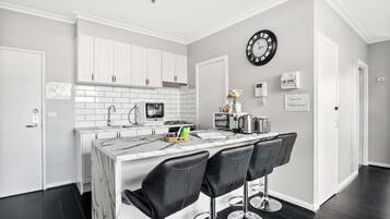 A modern kitchen with white cabinets, a marble island with bar stools, a clock, and a microwave.