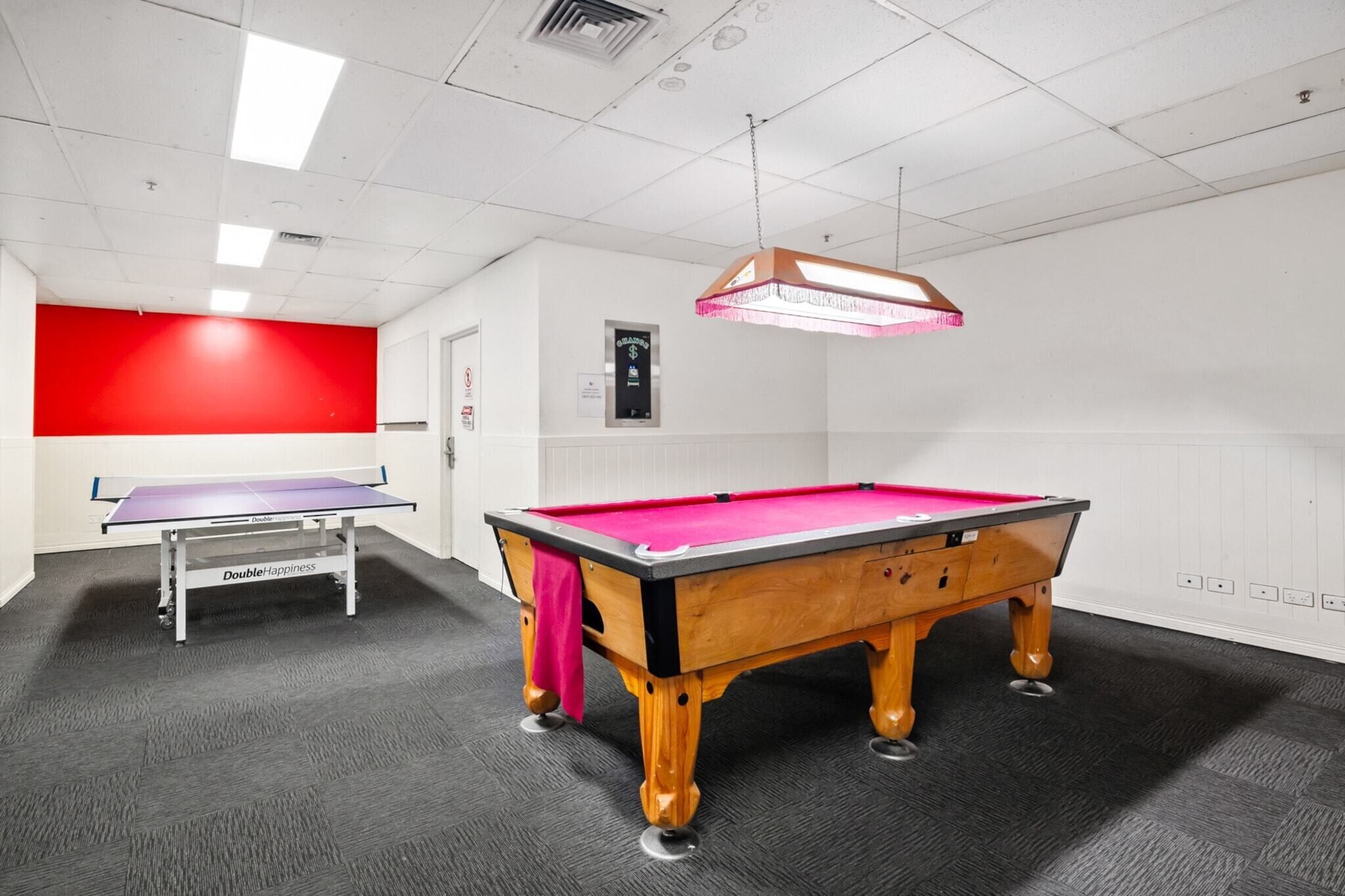 A pool table in a room with a red accent wall, a ping pong table, and a ceiling light fixture.
