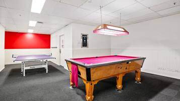 A pool table in a room with a red accent wall, a ping pong table, and a ceiling light fixture.