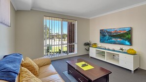 A living room with a sofa, coffee table, TV, and a large window with a view of the outdoors. - Spacious 3-Bed Home in Peaceful Byford (Byford)