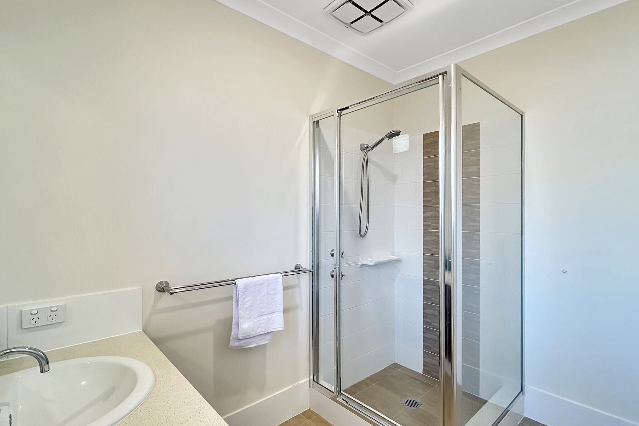 Un bany modern amb plat de dutxa envoltat de vidre, un lavabo blanc i una barra de tovalloles.