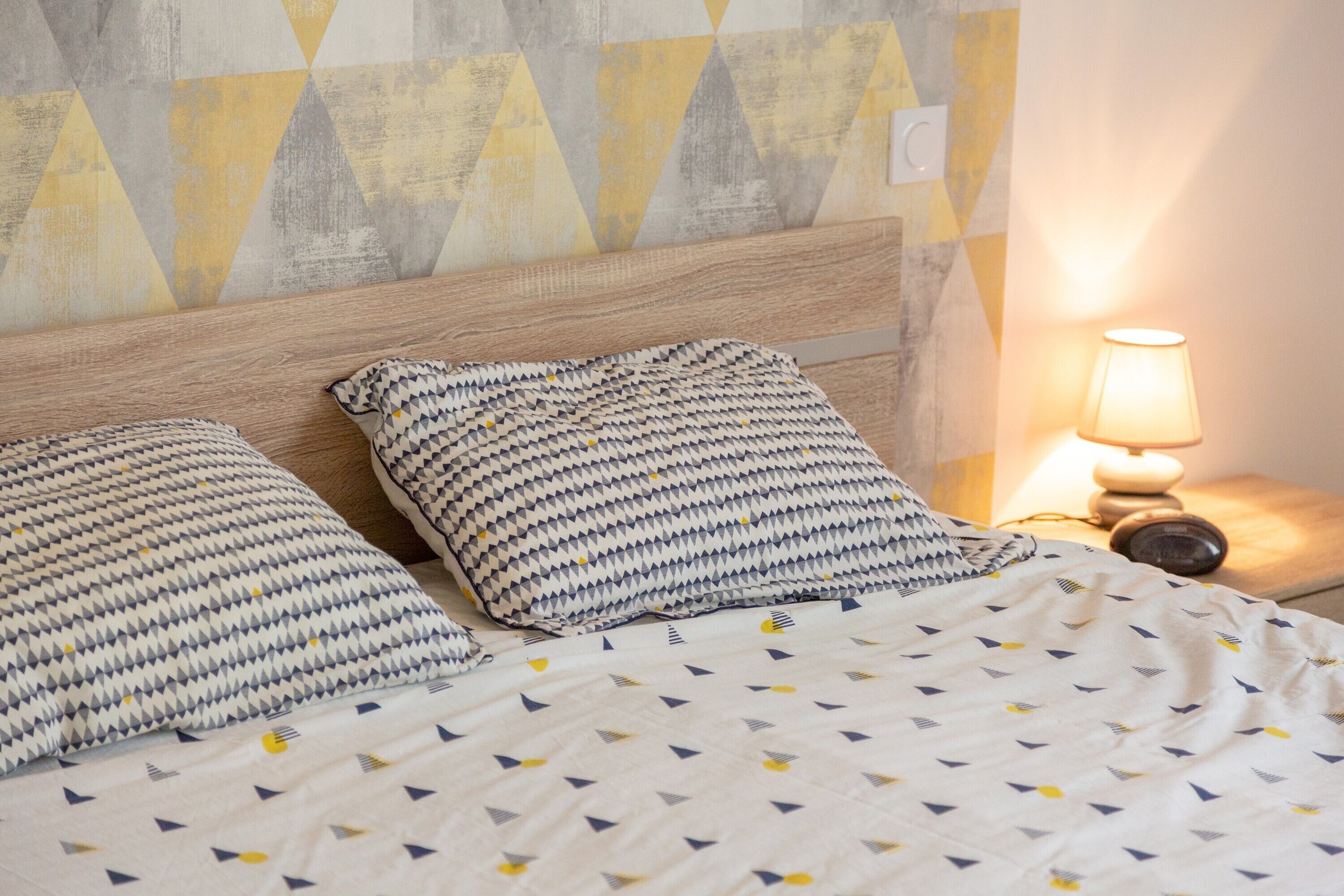 A bed with patterned bedding, a wooden headboard, and a bedside lamp.