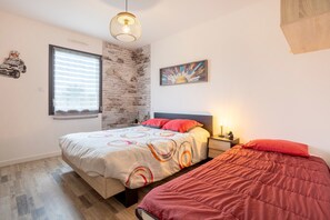 Une chambre à coucher comprenant un lit, une table de chevet, une fenêtre avec des stores, une œuvre d’art accrochée au mur et un luminaire suspendu.