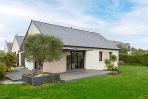 Une maison moderne avec un toit en pente, une grande porte d’entrée en verre et un jardin bien entretenu.
