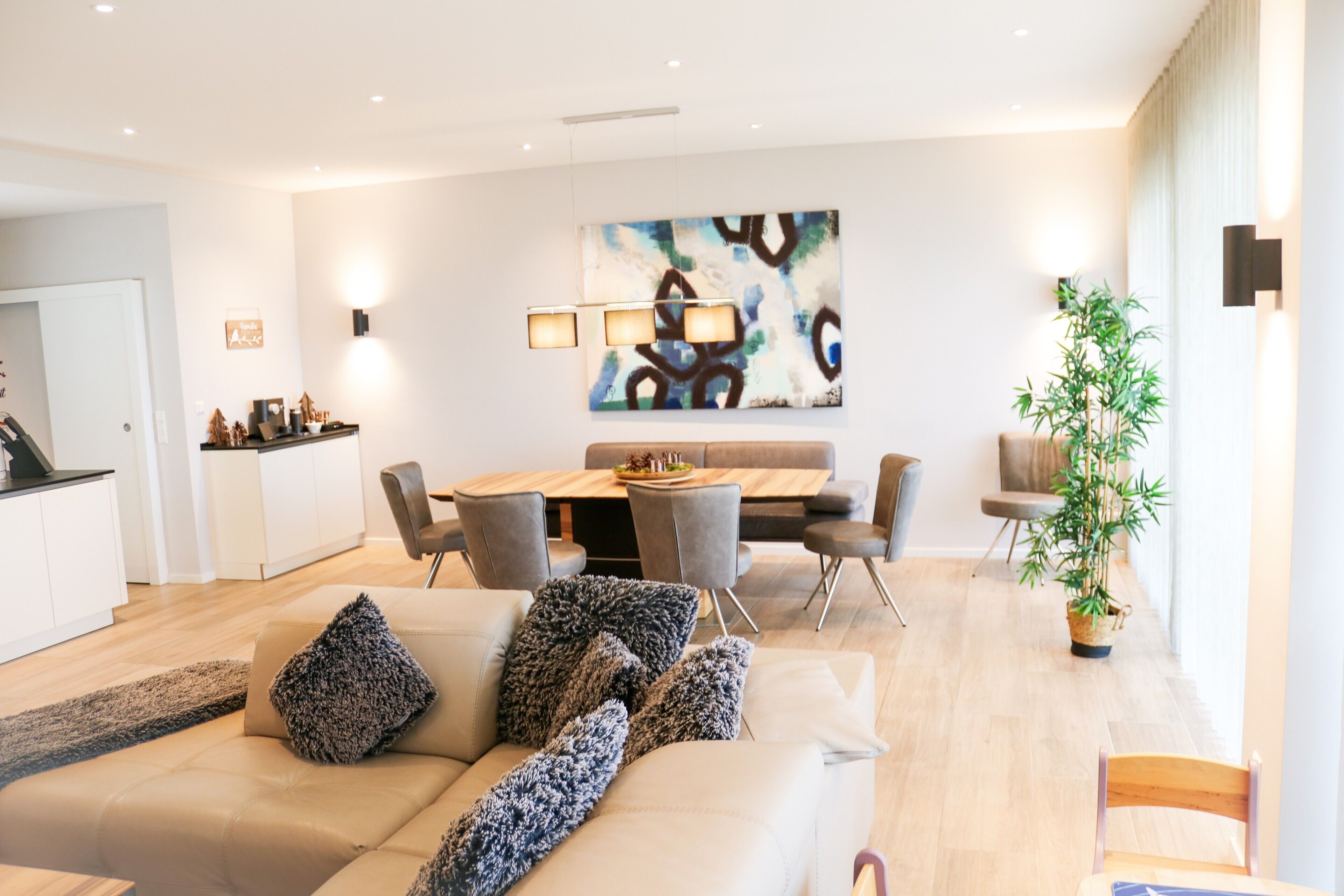 A modern living room with a sofa, dining table, chairs, and a large abstract painting.