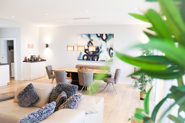 Un salon moderne avec un canapé, une table à manger et des chaises. Il y a un tableau au mur et une plante dans un coin.