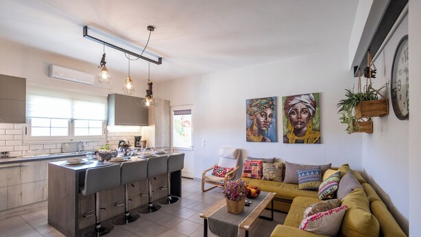 A modern kitchen with a bar area, a sofa, and a coffee table. There are two paintings on the wall and a clock. - 🏡 Paradiso Apartment | Full Air Conditioning • Outdoor Space • Near Corfu Town (Ionian Islands)