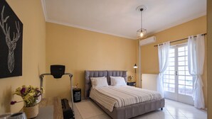 A bedroom with a large bed, a bedside table, a lamp, a window with curtains, and a wall-mounted air conditioner. - 🏡 Paradiso Apartment | Full Air Conditioning • Outdoor Space • Near Corfu Town (Ionian Islands)