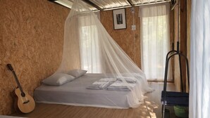 A bedroom with a bed under a mosquito net, a guitar, and a bunk bed in the background.