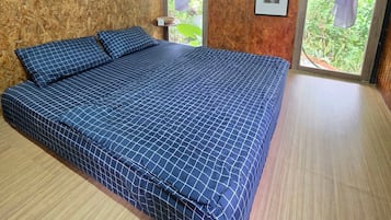 A room with a large bed, wooden walls, and a view of greenery through the windows.