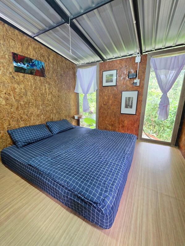 Una habitación con una cama grande, paredes de madera y vistas a la vegetación a través de las ventanas.