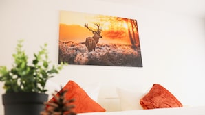 Un dormitorio con cama, almohadas, una planta en maceta y un cuadro de un ciervo en la pared.