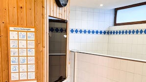 Zona de sauna con paredes de madera, un reloj y un cartel con instrucciones.