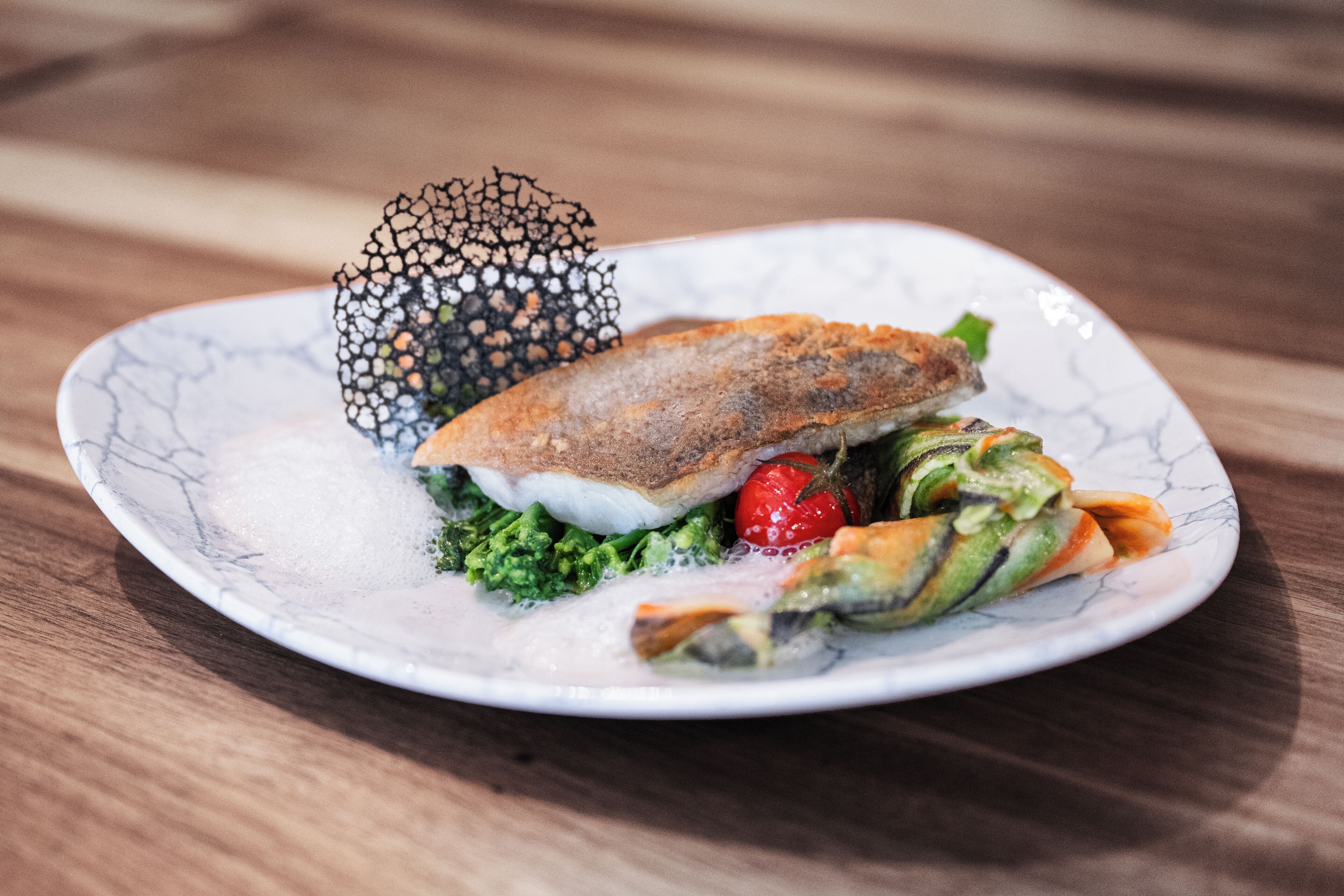 A plate with a fish sandwich, greens, and a decorative item.